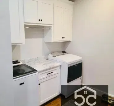 Laundry room with white cabinets, washer, dryer, and countertop.