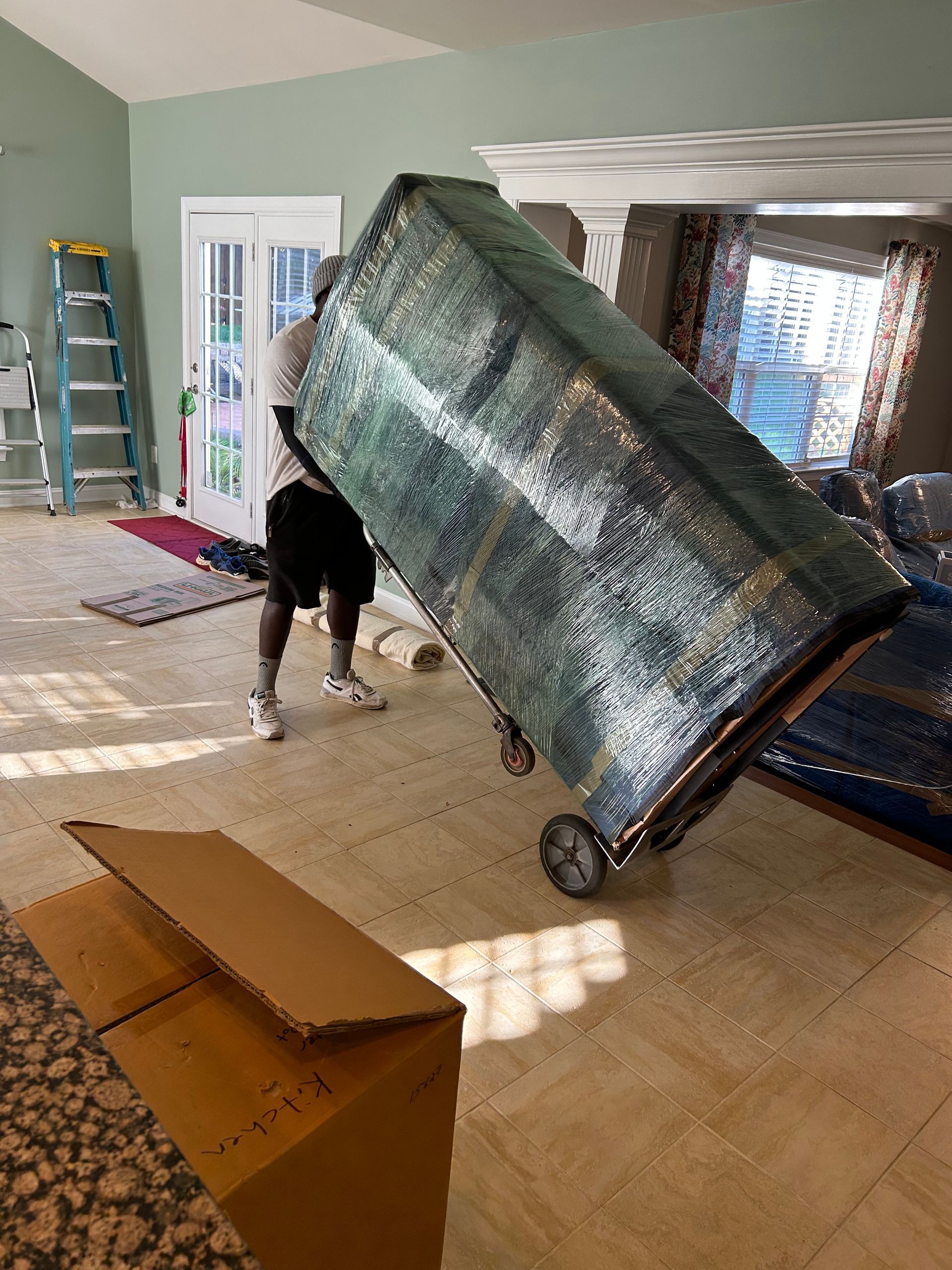 A man is carrying a large aquarium on a dolly in a living room.