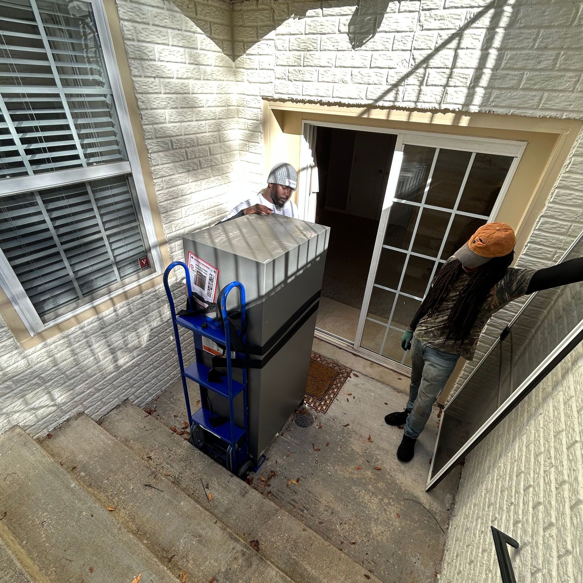 A man is pushing a box on a dolly down a set of stairs.