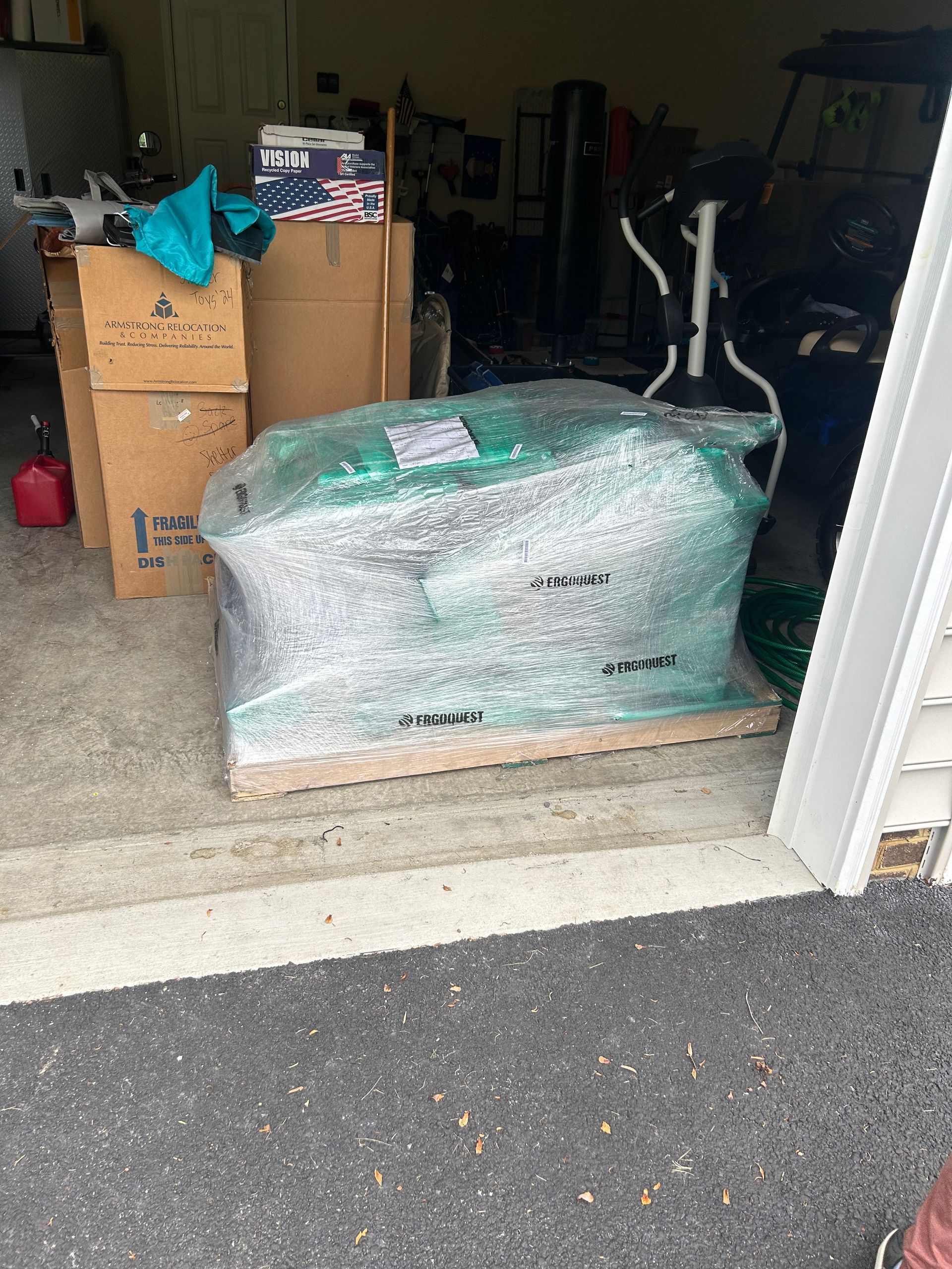 A large green object is wrapped in plastic and sitting on a wooden pallet in a garage.