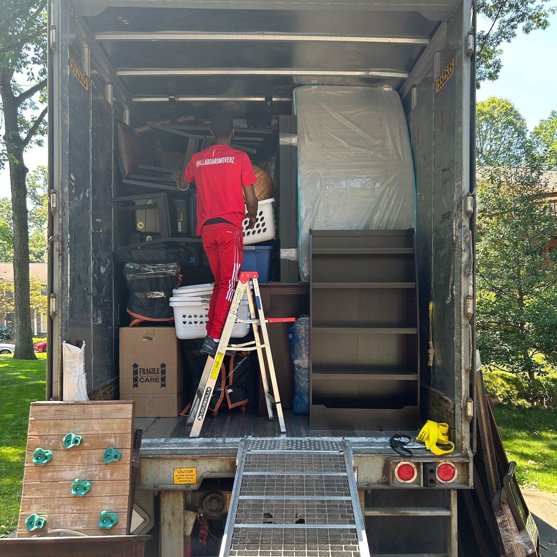 A man in a red shirt is standing on a ladder in the back of a moving truck