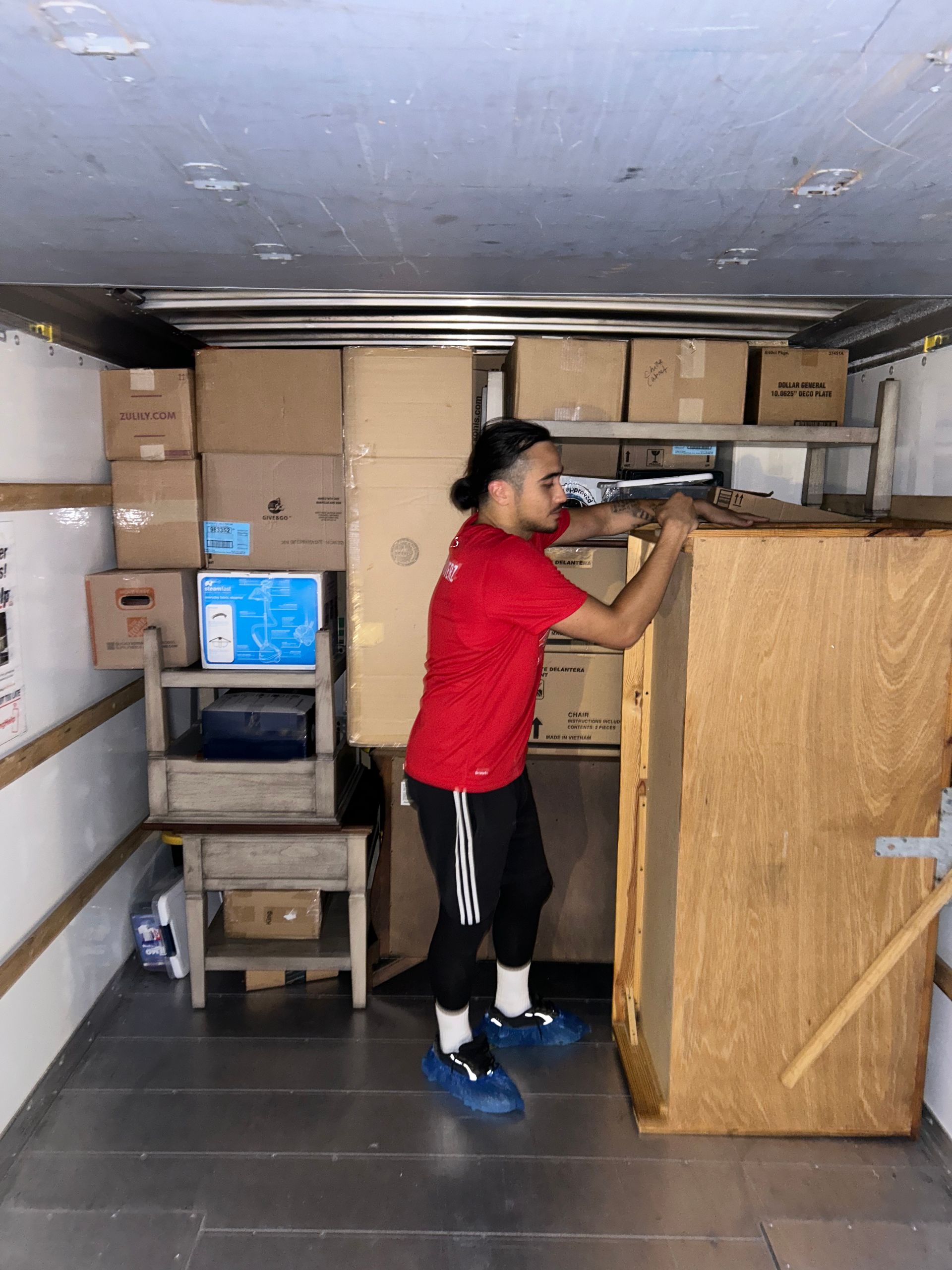 A man in a red shirt is standing in a room filled with boxes.