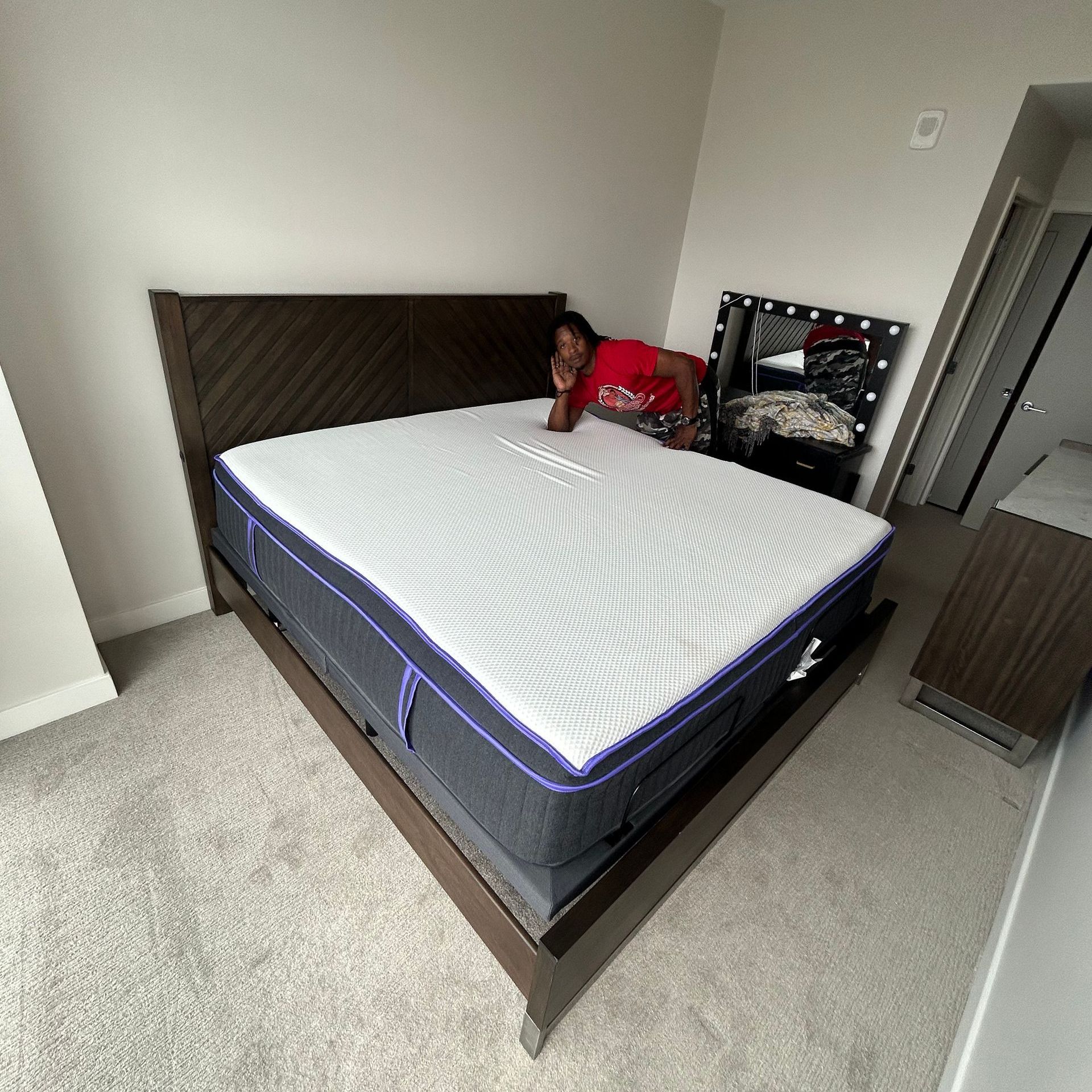 A man in a red shirt is standing next to a large mattress in a room.
