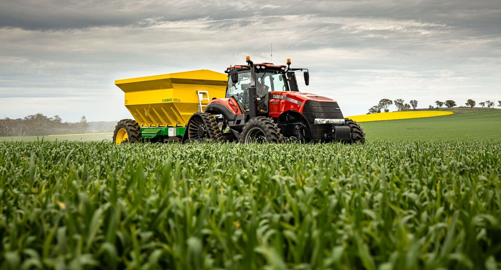 A red tractor is plowing a field of green grass.