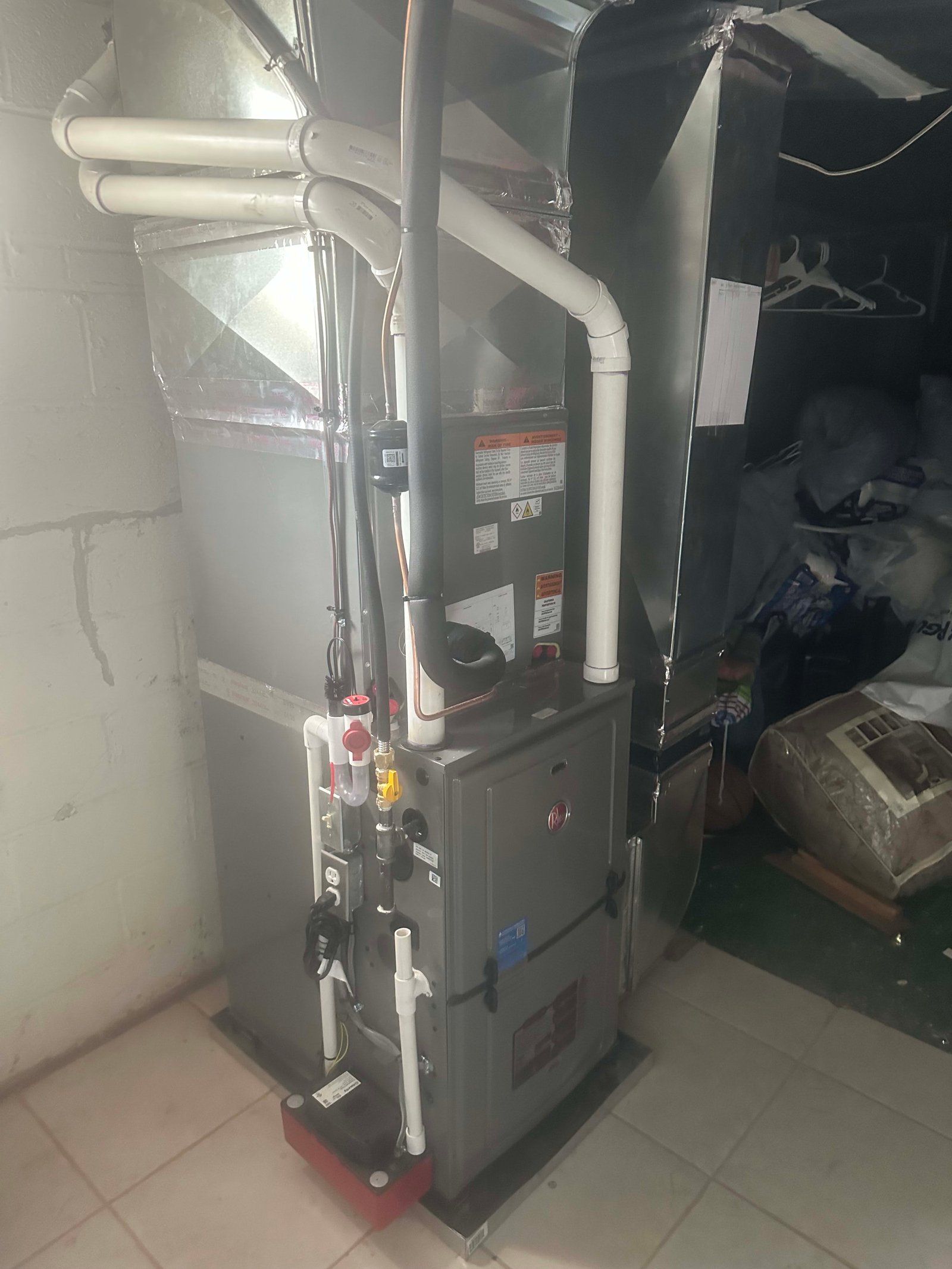 Furnace unit in a basement. Gray and silver metal with white pipes, against a concrete wall.