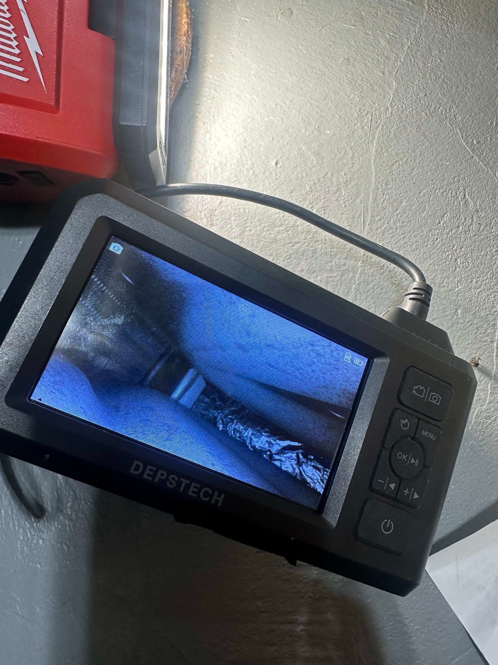 Defstech borescope screen showing a close-up view of a dark, narrow space with a black handle and control buttons.