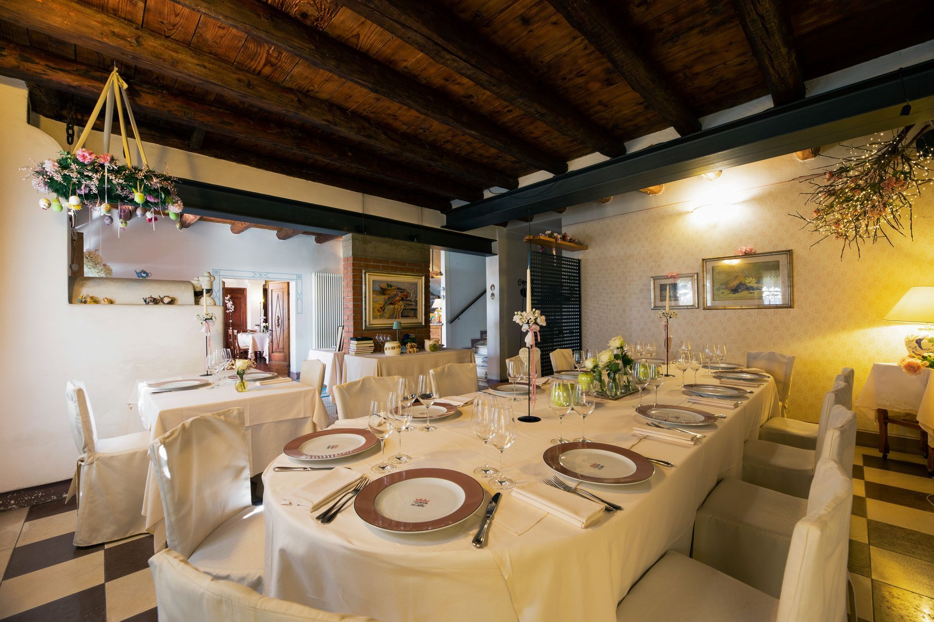 Sala da pranzo formale con lungo tavolo apparecchiato per un pasto. Tovaglia bianca, sedie e centrotavola floreale.