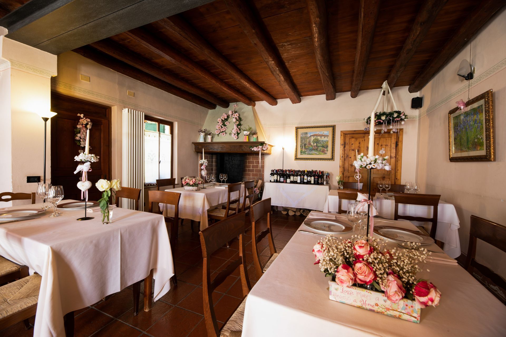 Sala da pranzo del ristorante con tavoli apparecchiati per il pasto, camino e soffitto con travi in legno.