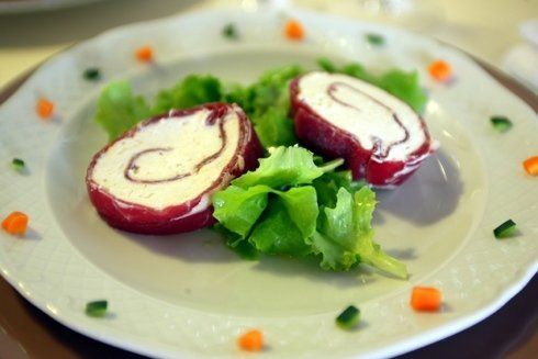 Due antipasti di carne arrotolata con ripieno bianco, serviti su lattuga. Piatto bianco con guarnizione di carote e cetrioli.