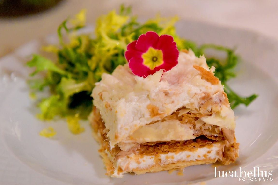 Un dessert a strati con crema bianca e pasta sfoglia dorata, guarnito con un fiore rosso, servito con insalata verde.
