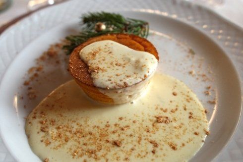 Dessert a forma di muffin con crema pasticcera, guarnito con spezie e un rametto di sempreverde su un piatto bianco.