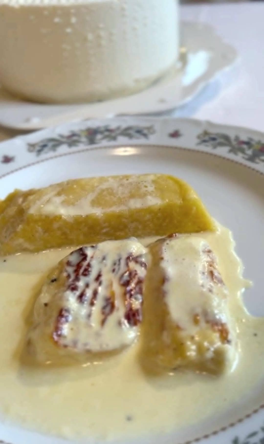 Piatto di cibo con salsa cremosa e una forma di formaggio sullo sfondo.