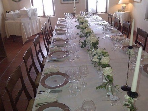 Lungo tavolo da pranzo apparecchiato per un evento formale con fiori bianchi, candele e posate.