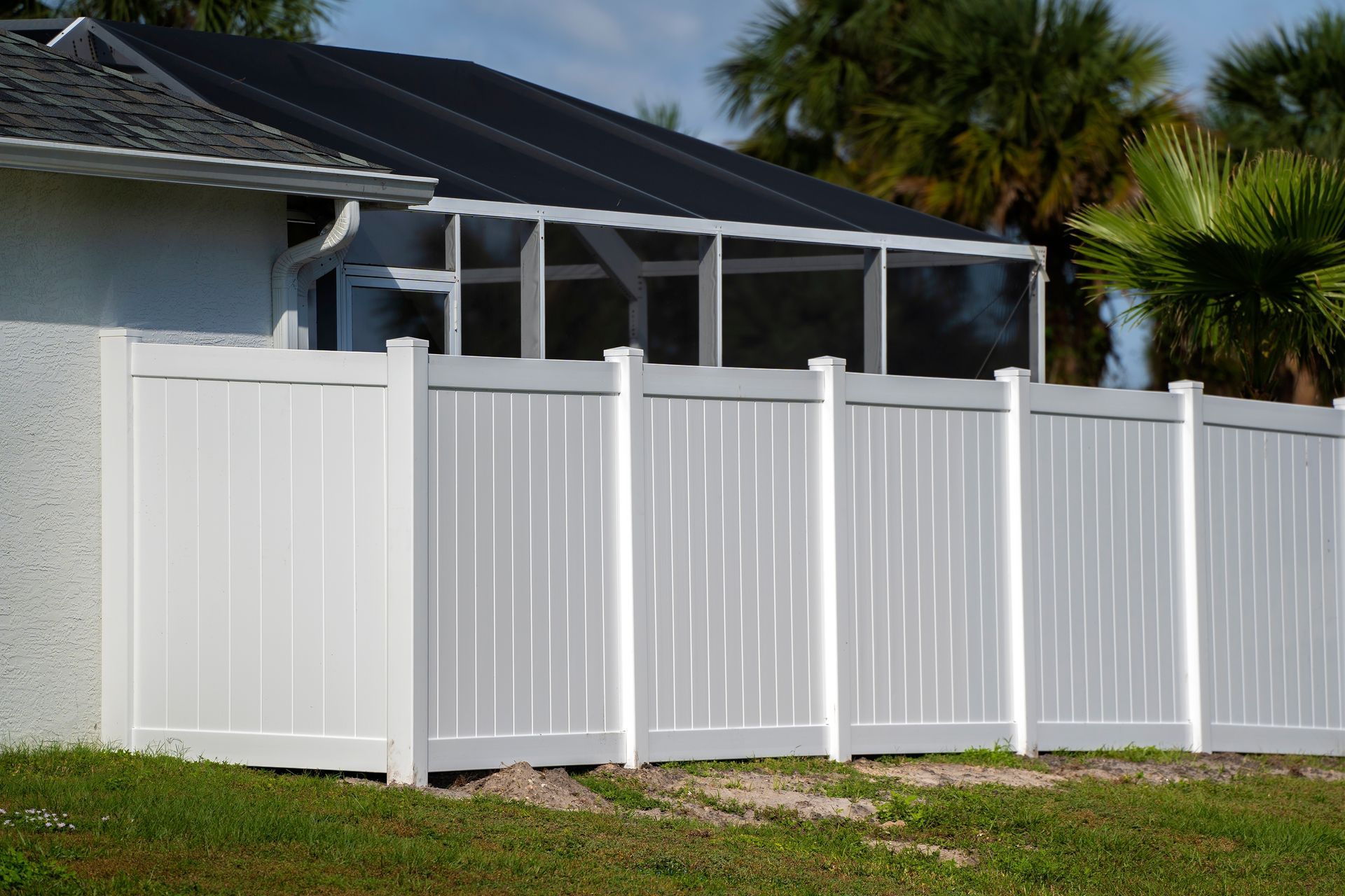 White vinyl fence with gates in front of a house and screened patio.