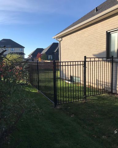 Black metal fence encloses a small yard next to a beige brick house.