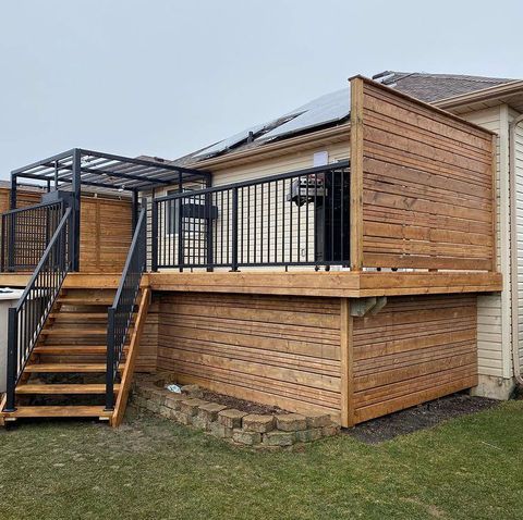 Wooden deck with black railing and stairs attached to a house with solar panels.