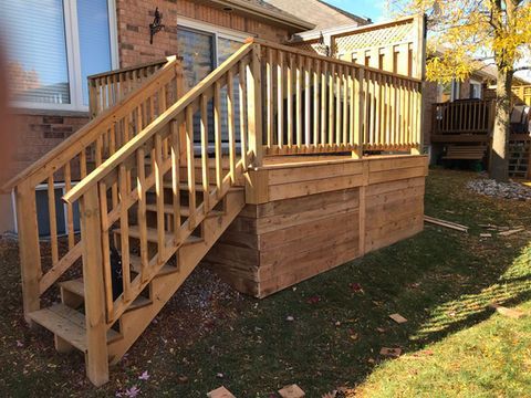 Wooden deck with stairs, built against a brick house with a green lawn.