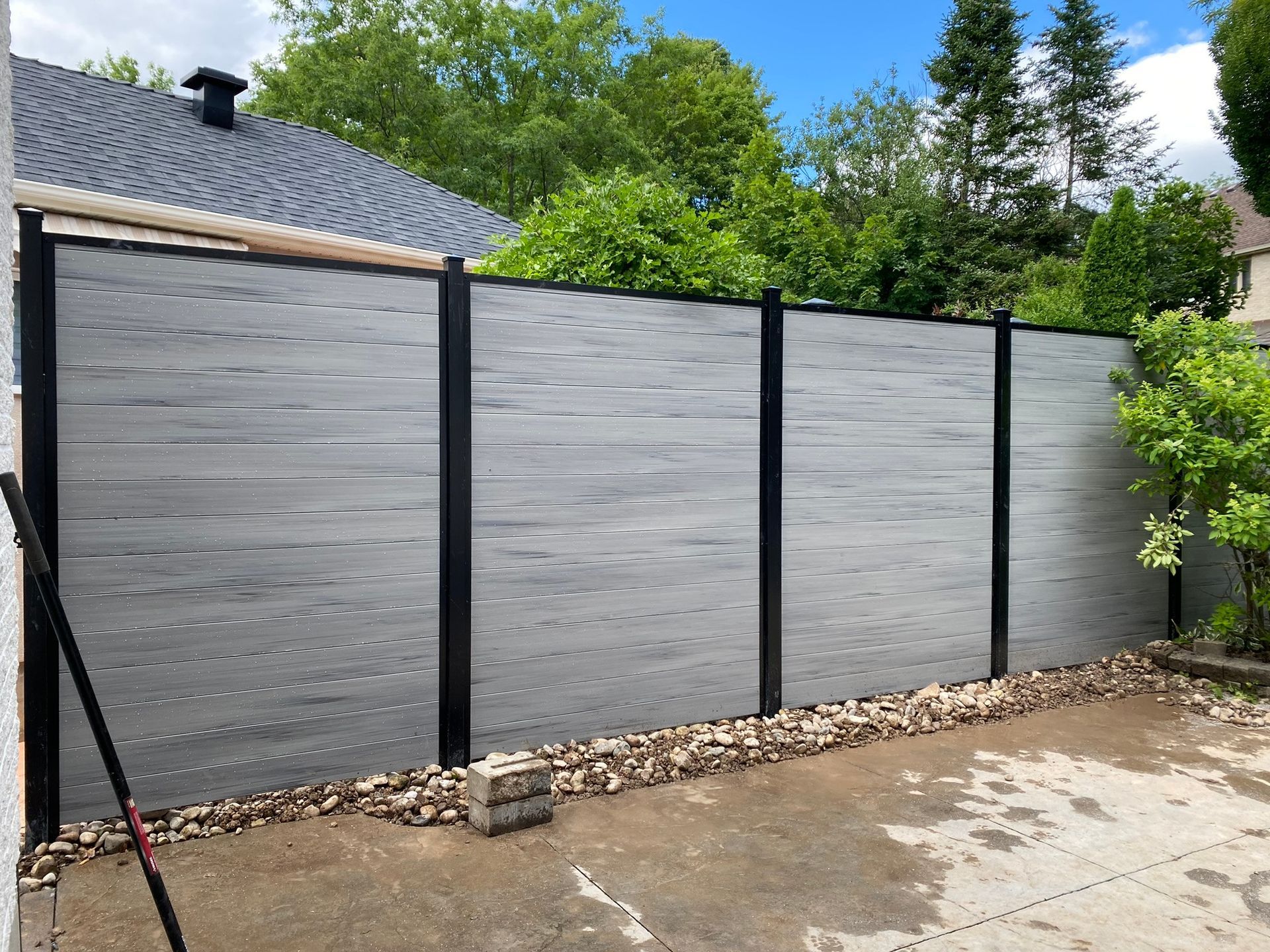 Gray horizontal composite fence with black posts in a yard.