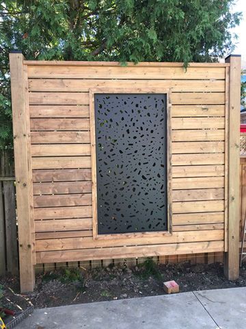 Wooden fence with a dark, patterned panel in the center. Light brown wood, outdoor setting.