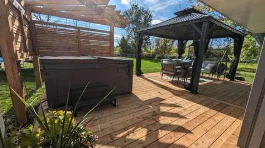 Wooden deck with hot tub and gazebo in sunny outdoor setting.