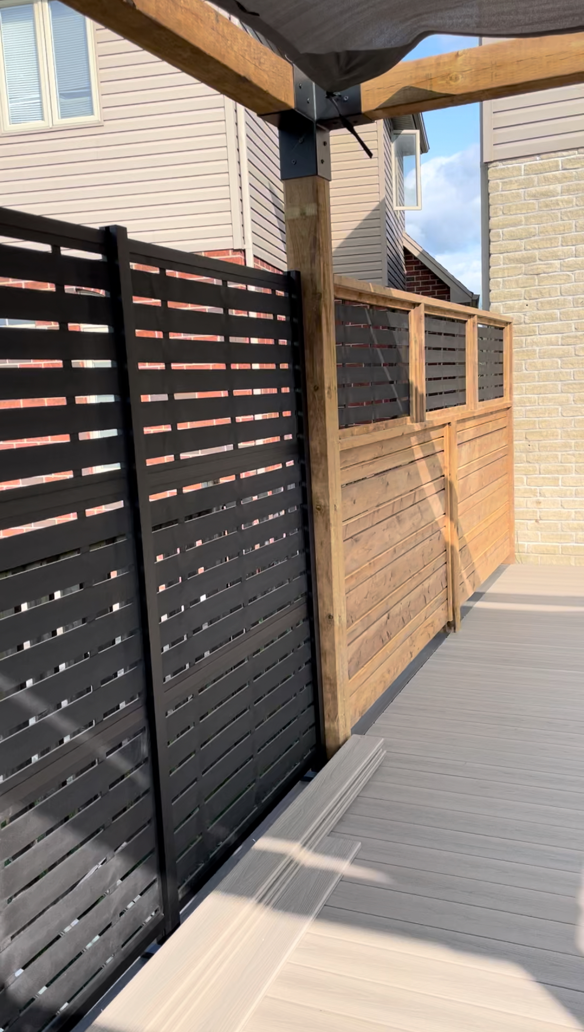 Outdoor walkway with black slatted and wooden privacy screens under a shaded pergola