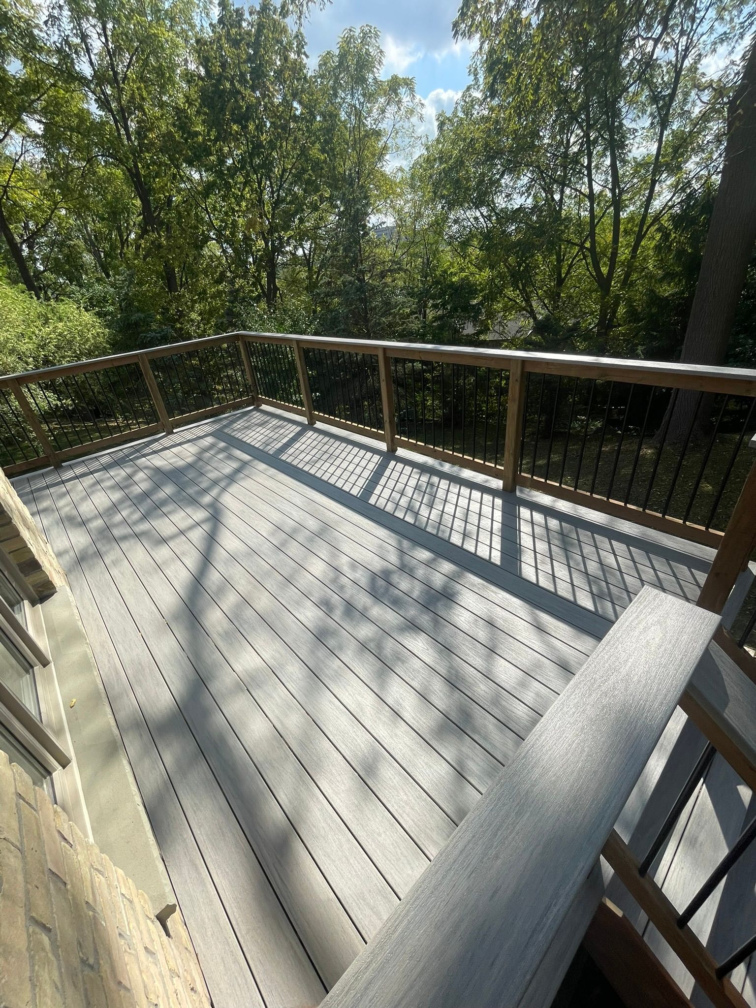 Sunny wooden deck with railing, surrounded by trees and dappled shadows.