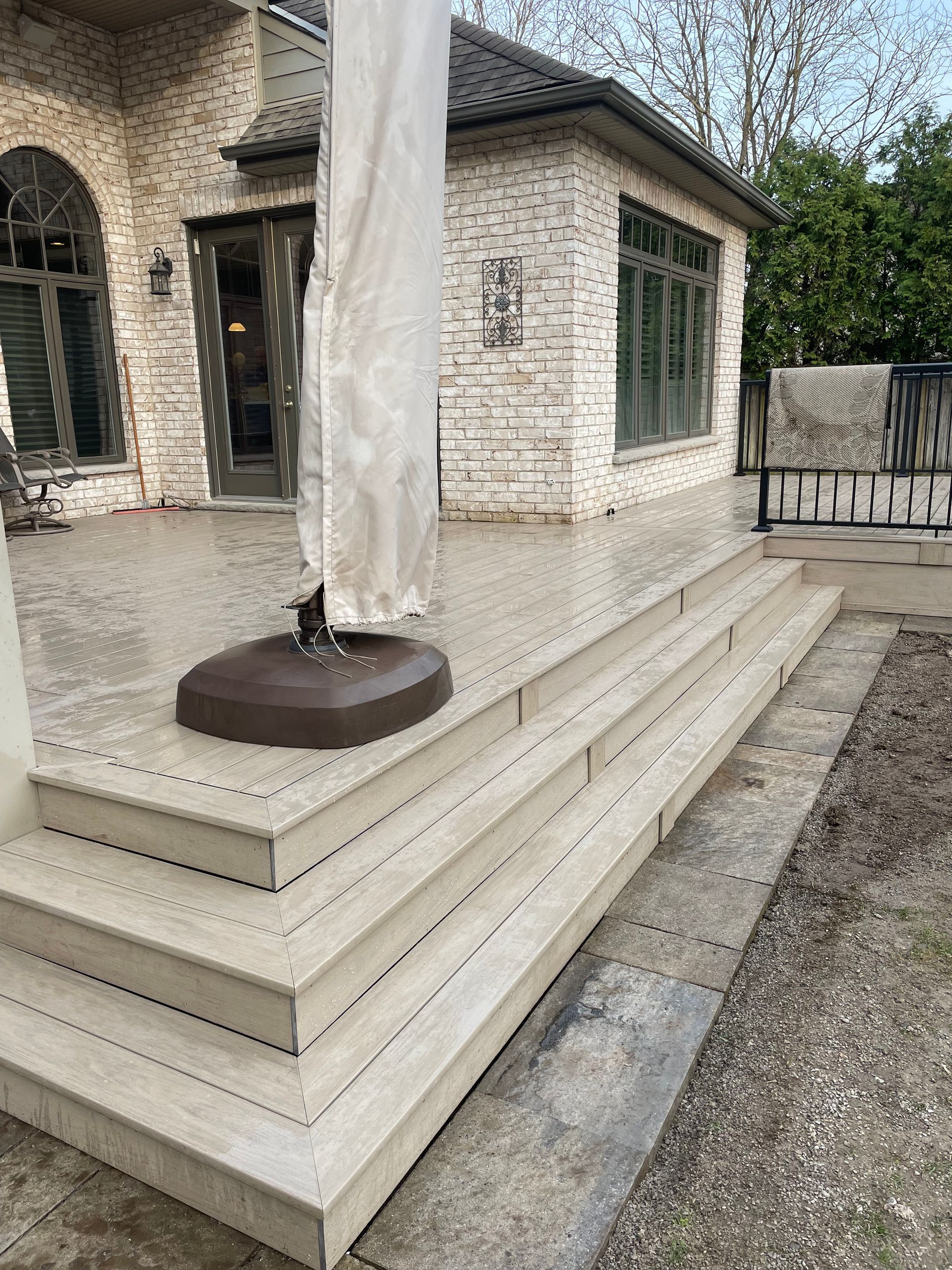 Cream-colored deck stairs beside a stone house, with a closed patio umbrella on the landing.