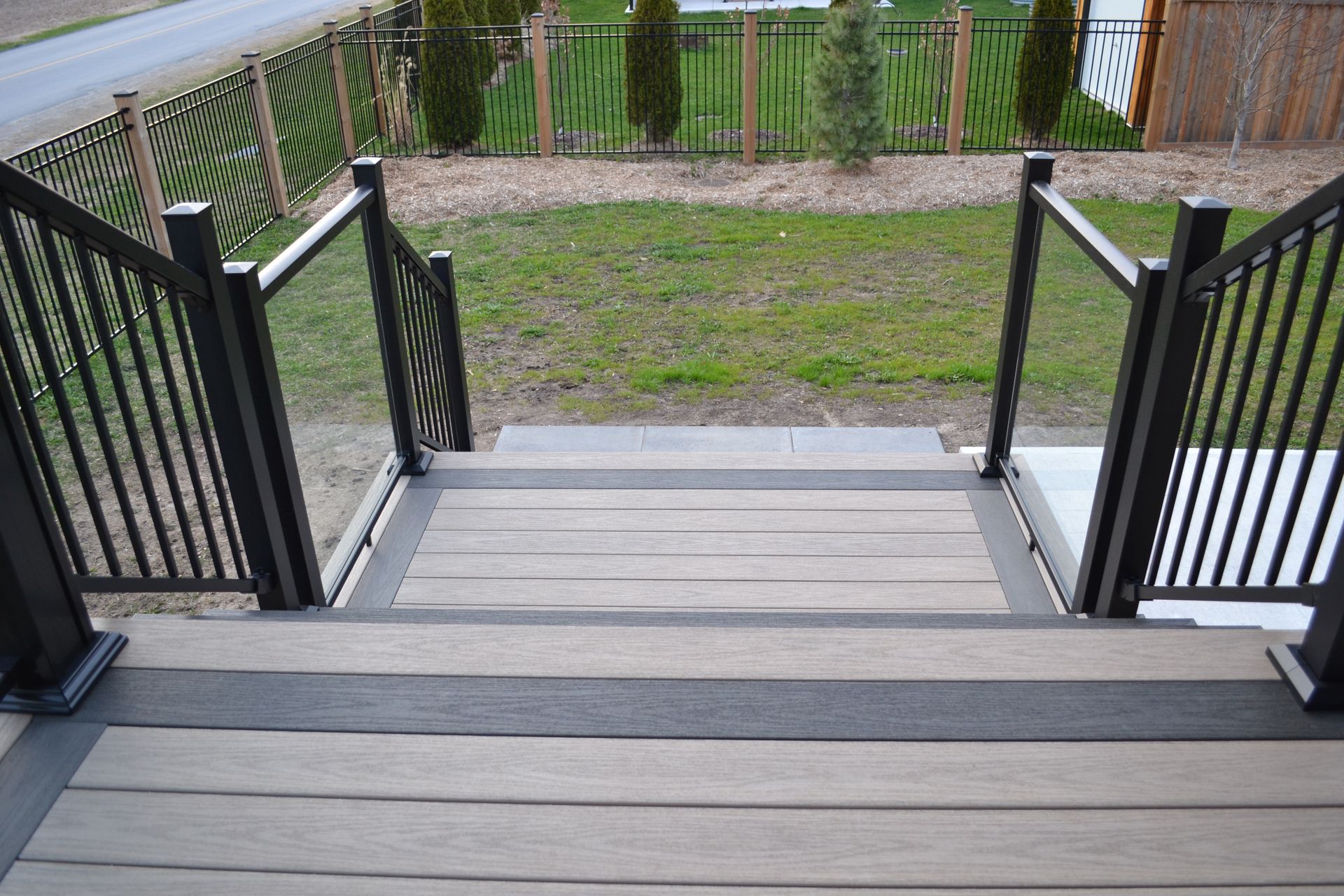 Front steps with black railings leading down to a gravel path and grassy yard.