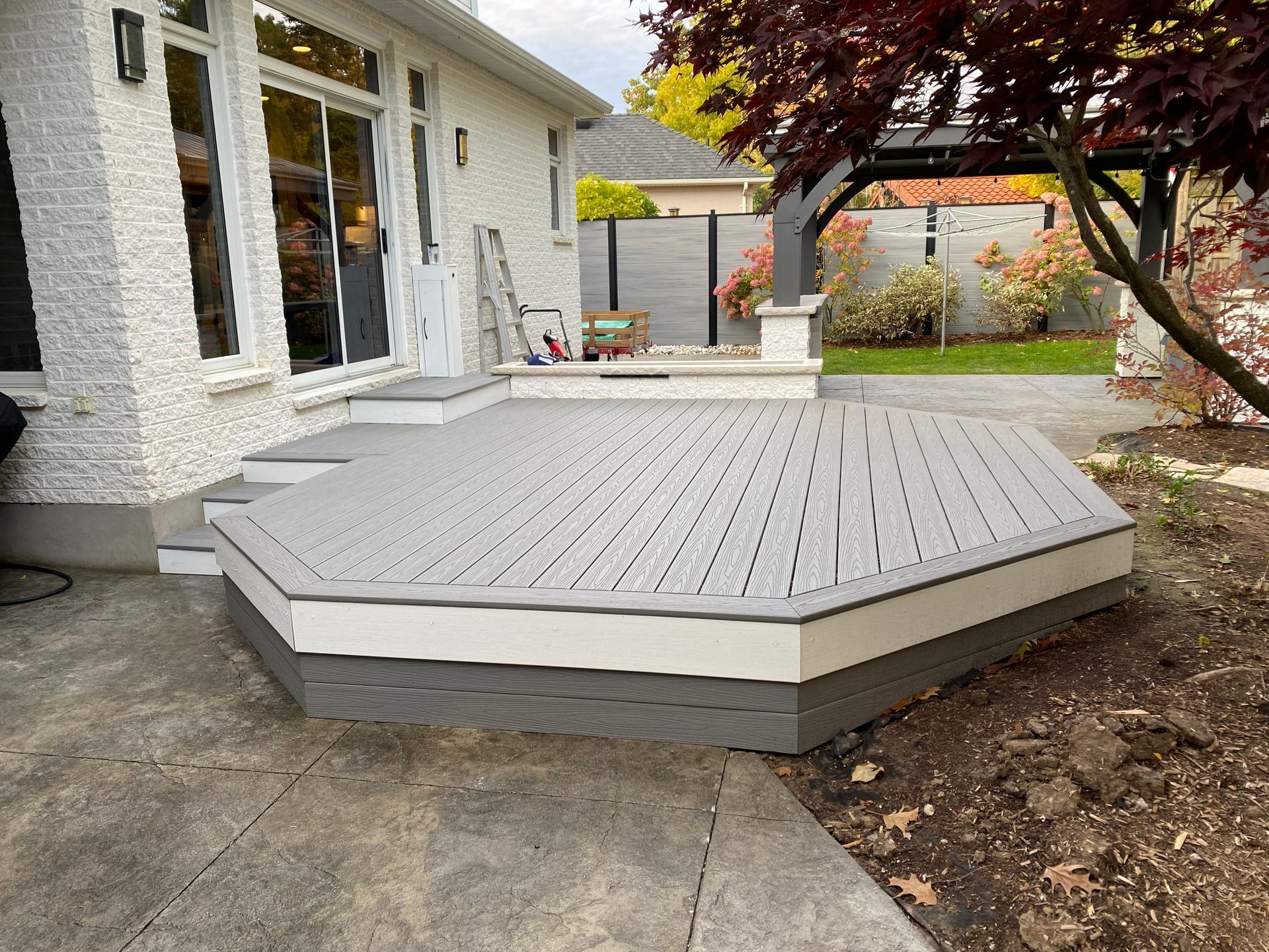 Octagonal gray wooden deck beside a white house in a backyard