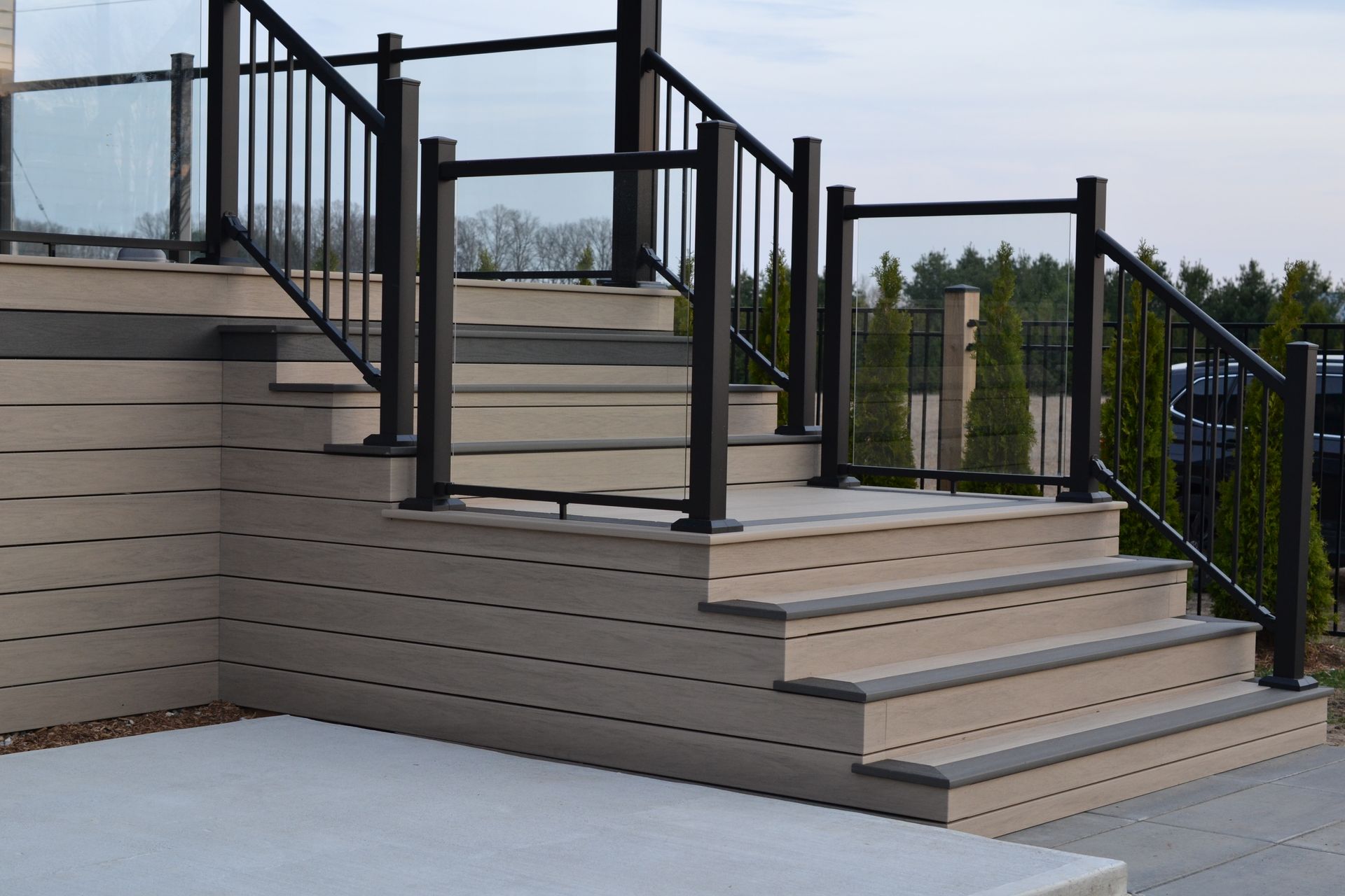 Composite deck stairs with black railing and glass panels.