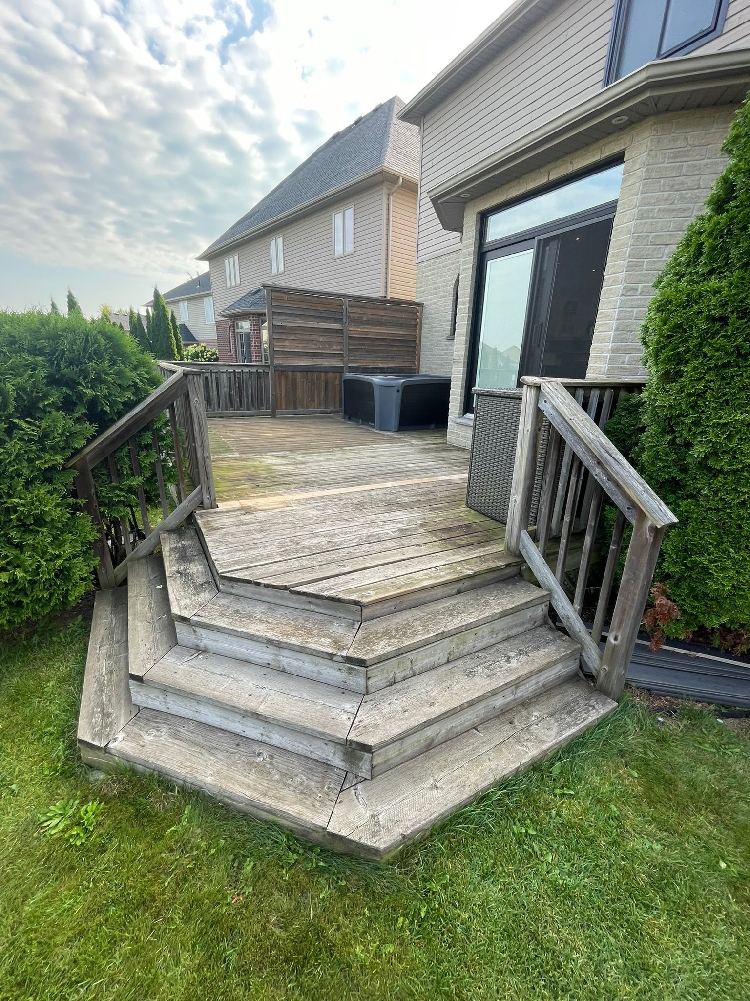 Concrete steps and wooden deck leading to a house, surrounded by grass and shrubs.