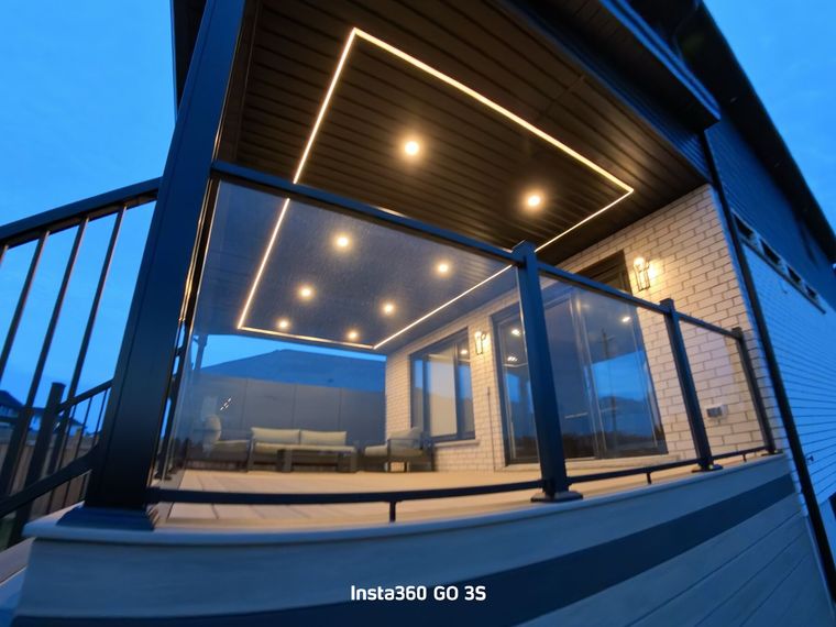 Lit outdoor deck with glass railing, black trim, and modern lighting. Evening view.