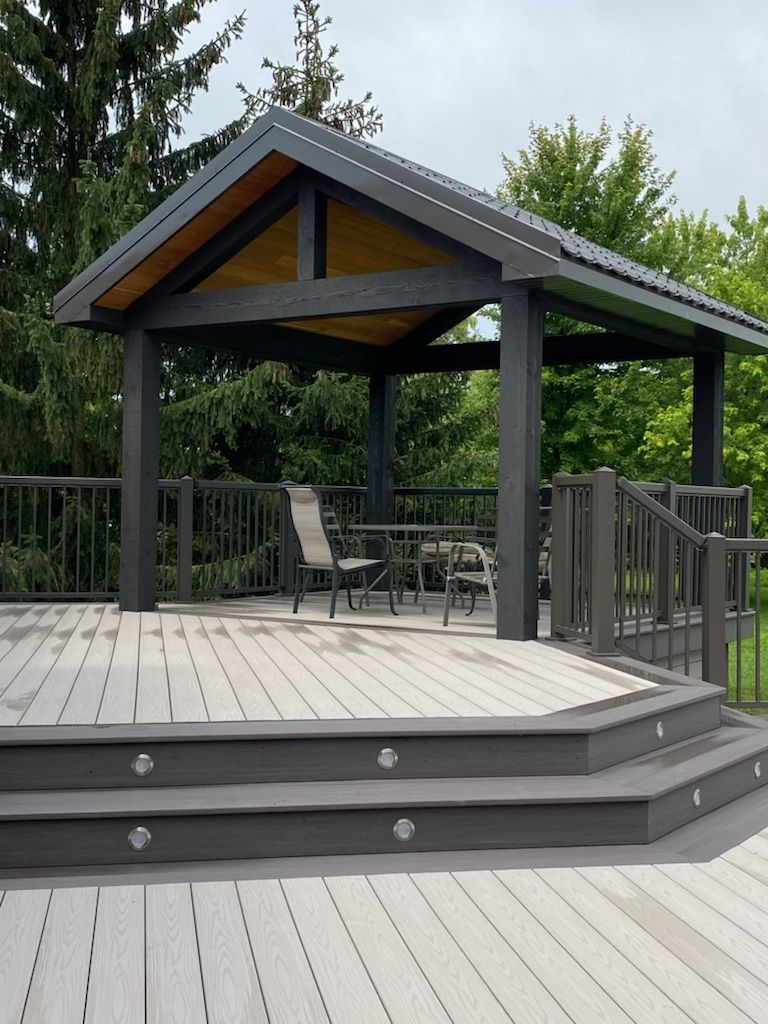 Gray deck with gazebo, steps, and seating area. Outdoor setting with trees.