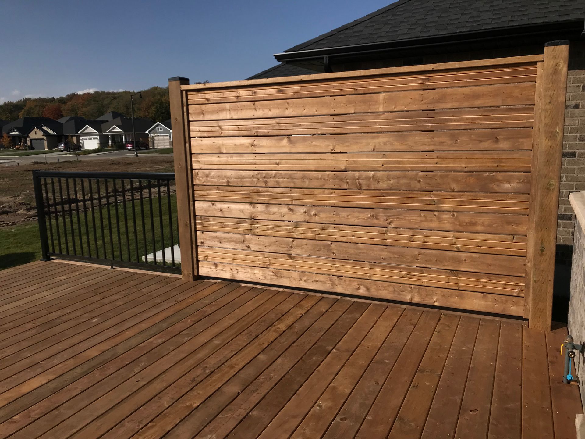 Wooden privacy screen on a deck. Brown planks, black railing, blue sky.
