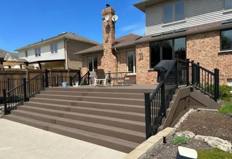 Composite deck with multiple steps, black railings, attached to a brick house. Blue sky.