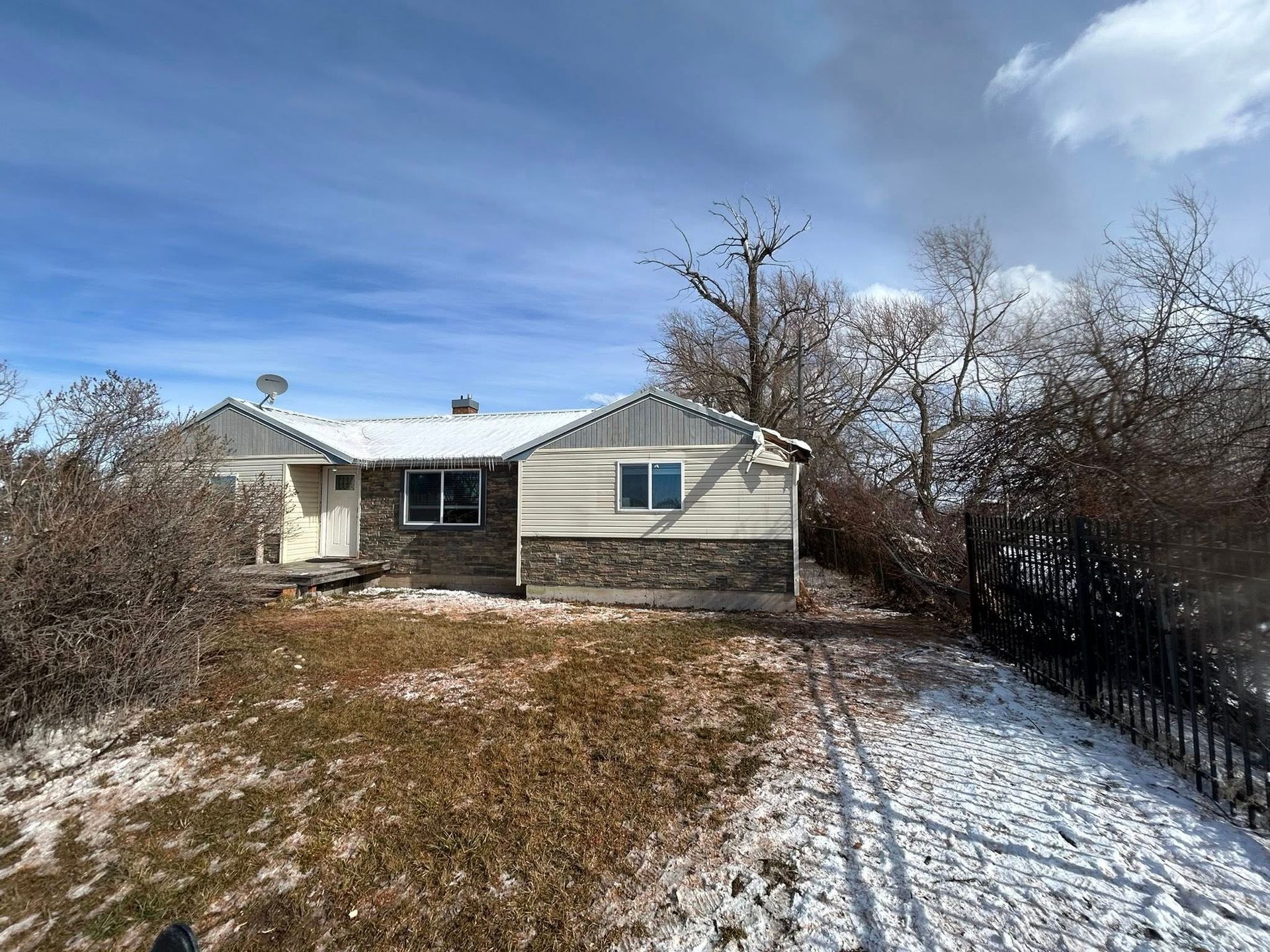 Small beige house with leafless trees and a snowy yard under a blue sky