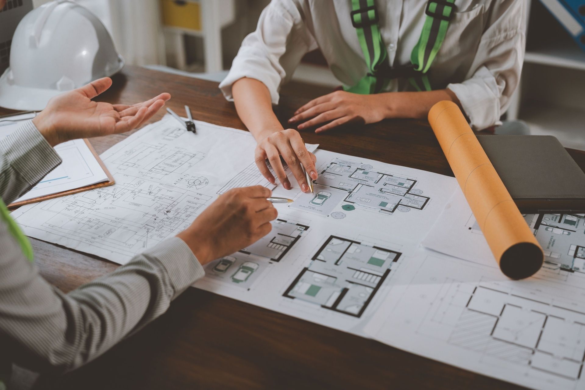 People reviewing architectural floor plans and sketches on a table with rolled blueprint plans