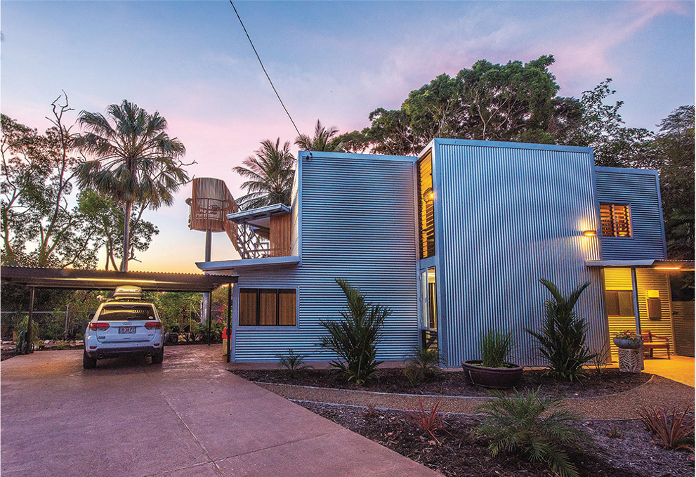 Modern house with corrugated metal siding, carport, and car. Evening light.