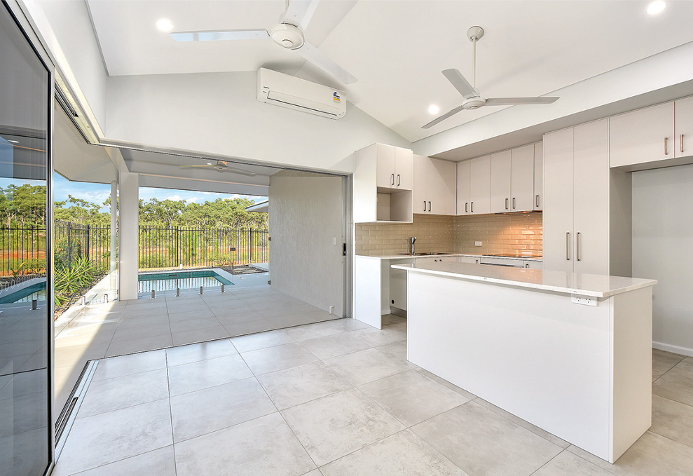 Bright kitchen with white cabinets, opens to a patio with a pool.