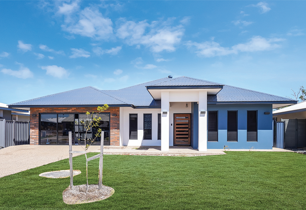 Modern one-story house with blue roof, white and blue walls, brown front door, green lawn under a blue sky.