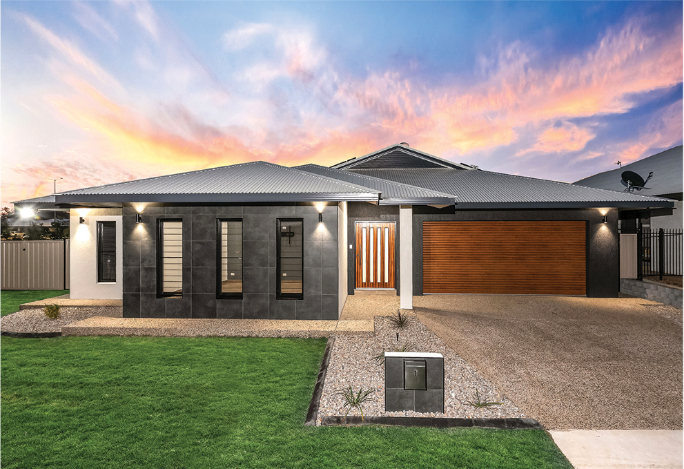 Modern house with gray facade, wooden garage door, and green lawn under a sunset sky.