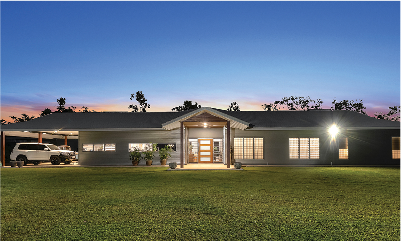 Ranch-style house at dusk with a car in the carport; a well-lit front entrance and lawn.