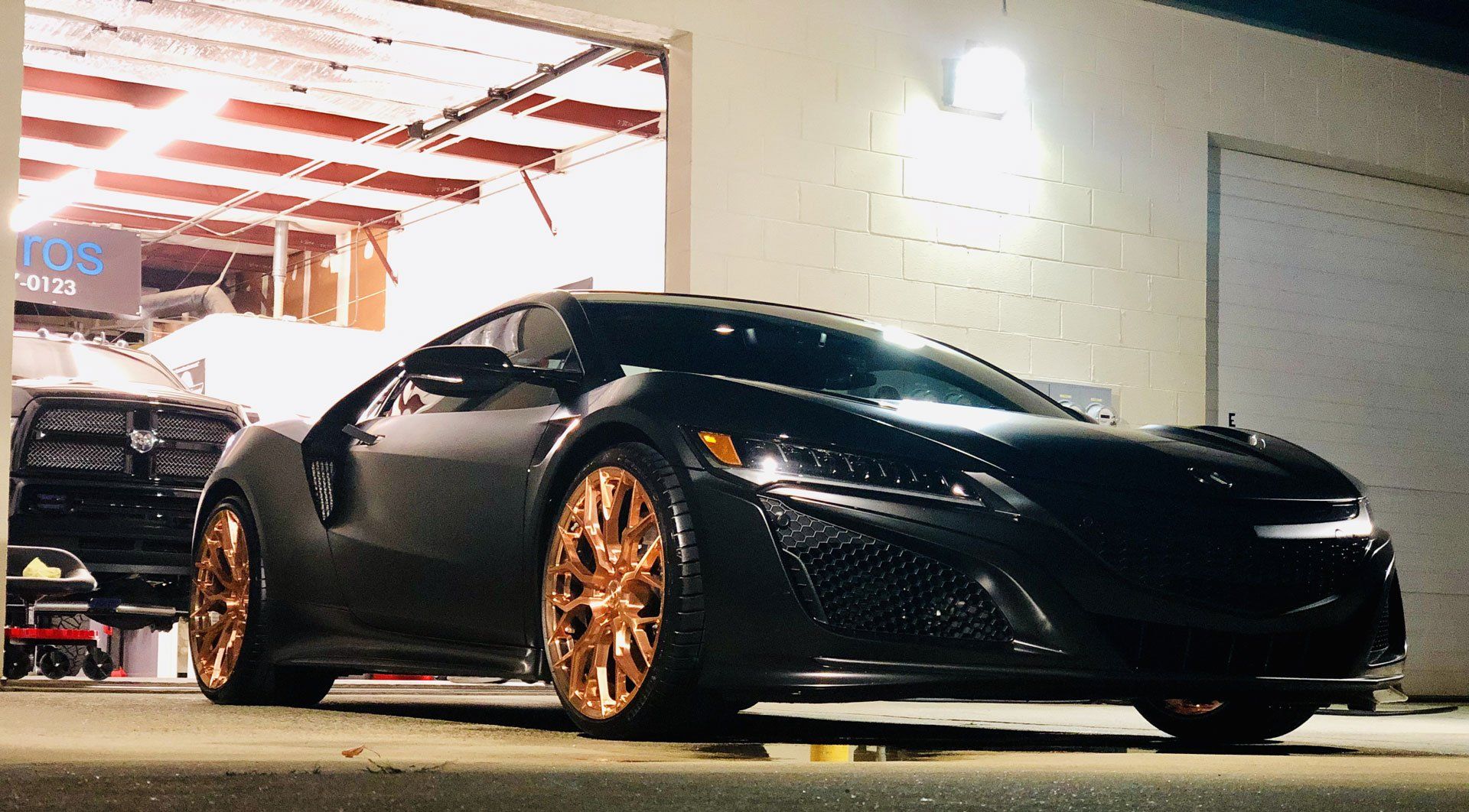 A black sports car is parked in front of a garage at night.