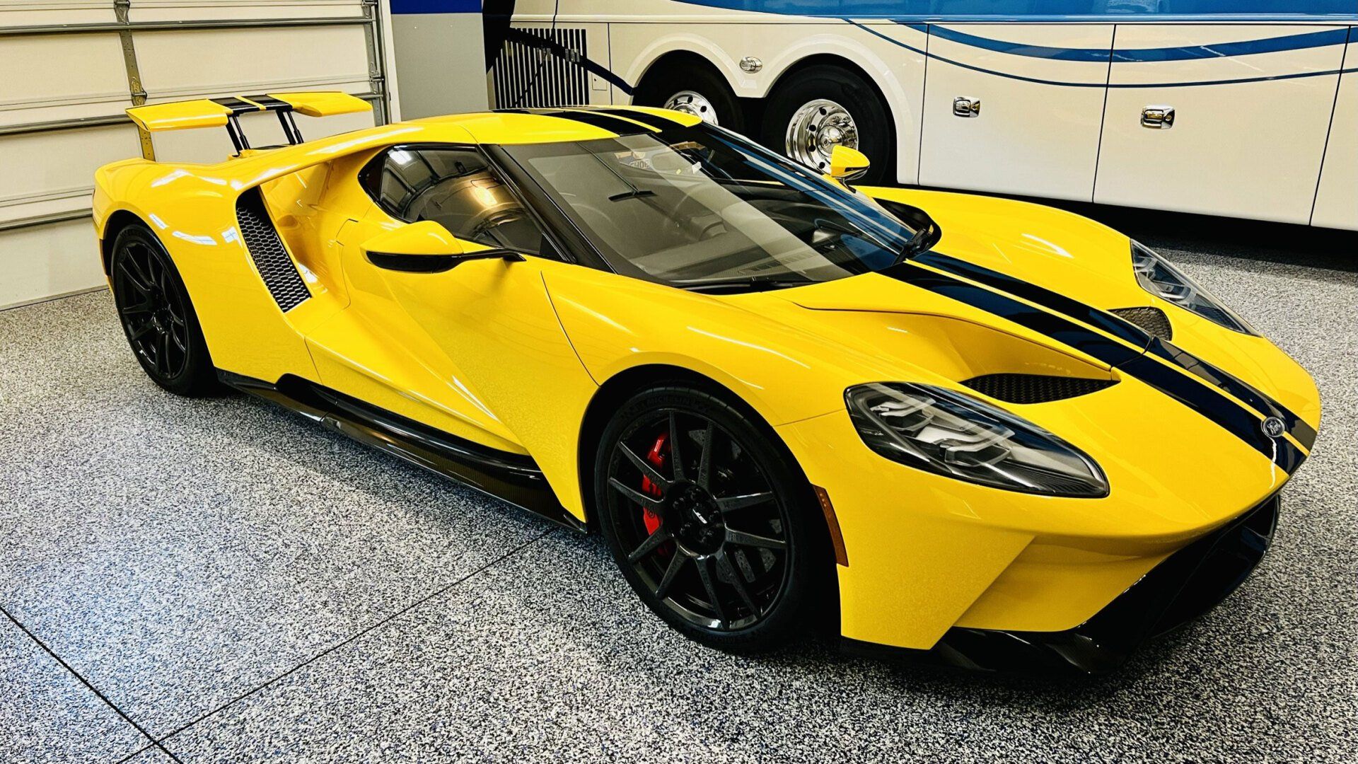 A yellow sports car is parked in a garage next to a trailer.