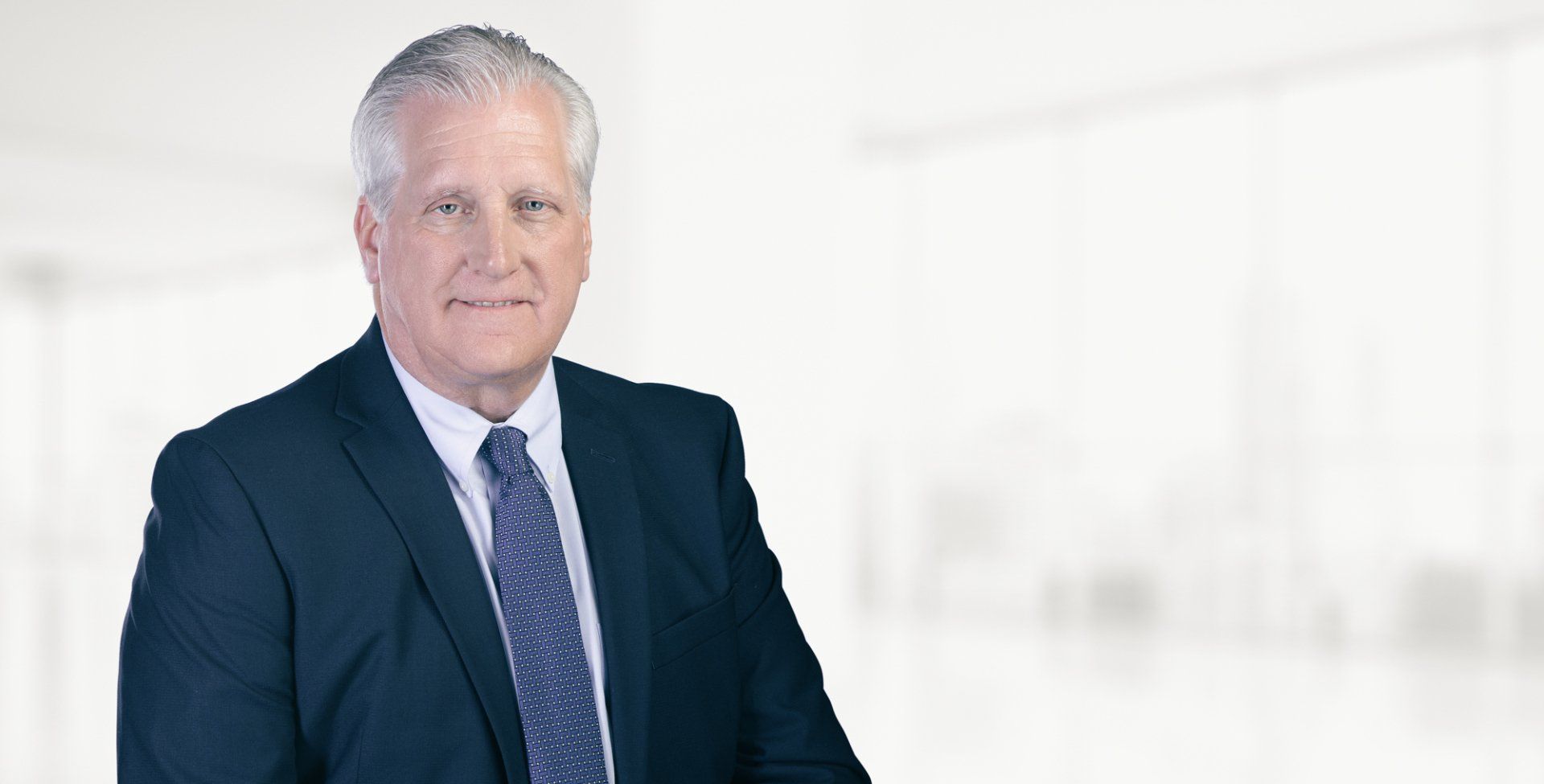 A man in a suit and tie is standing in front of a white wall.