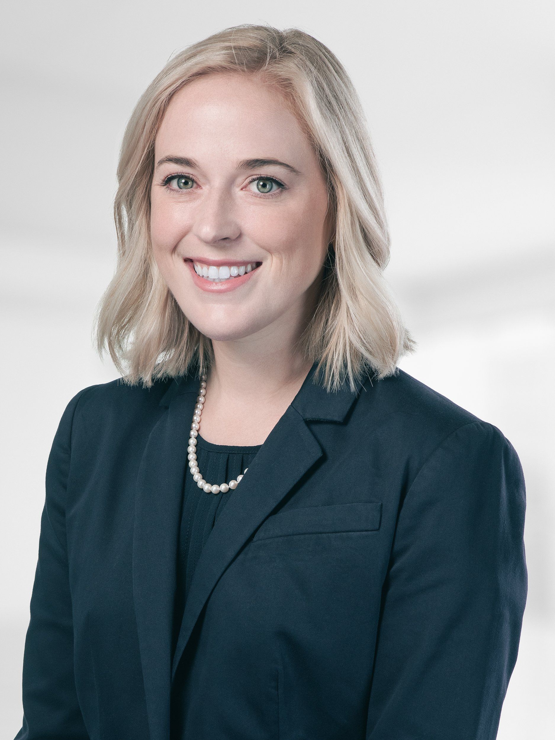 A woman in a suit and pearl necklace is smiling for the camera.