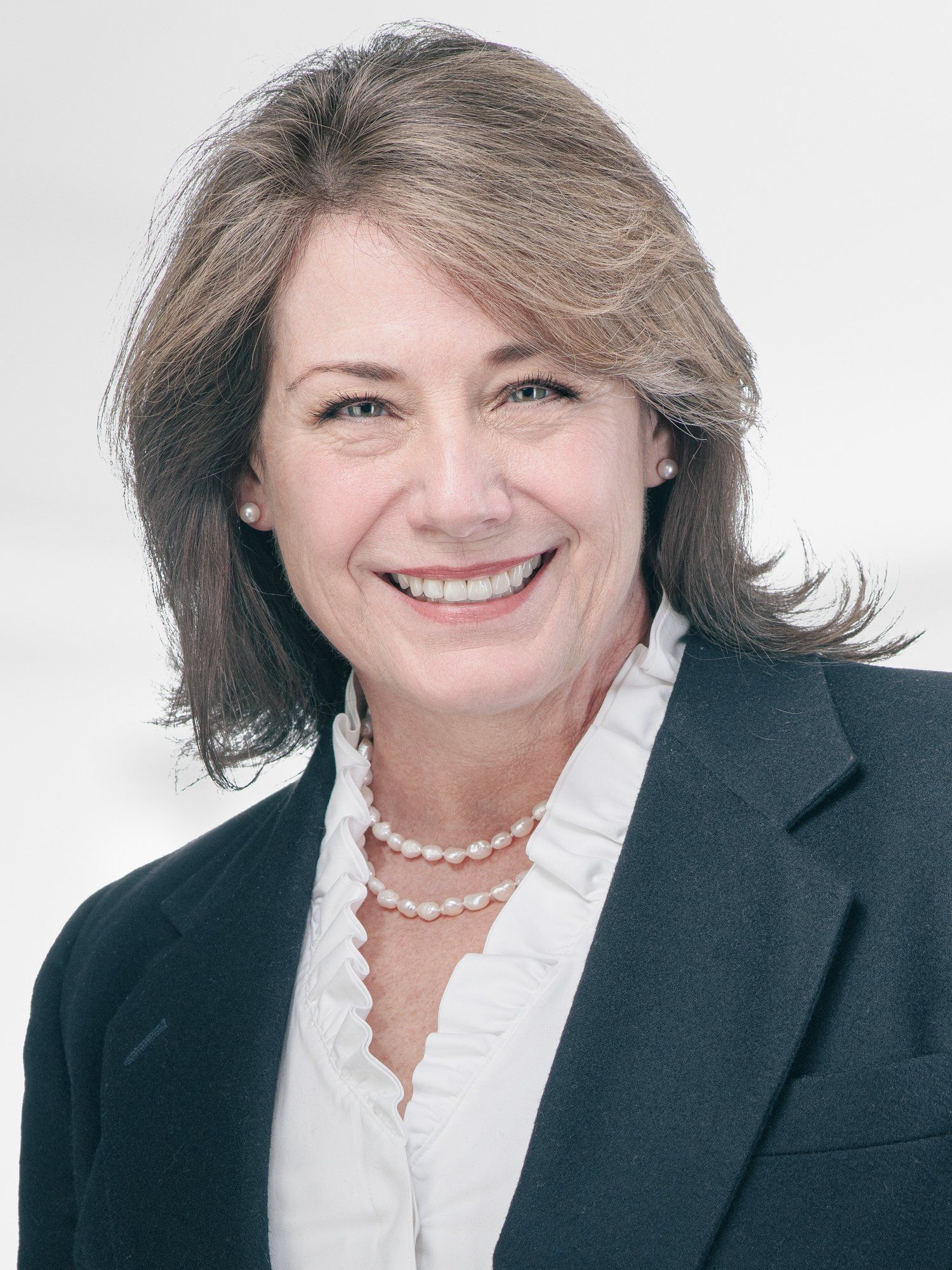 A woman wearing a suit and a pearl necklace smiles for the camera.