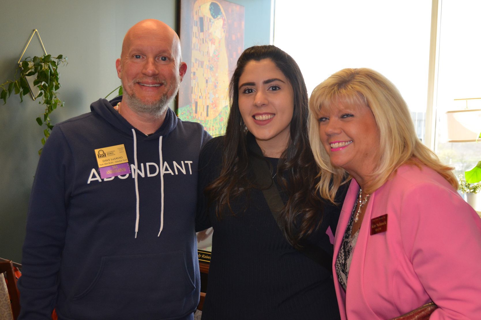 A man and two women are posing for a picture . the man is wearing a sweatshirt that says abundant.