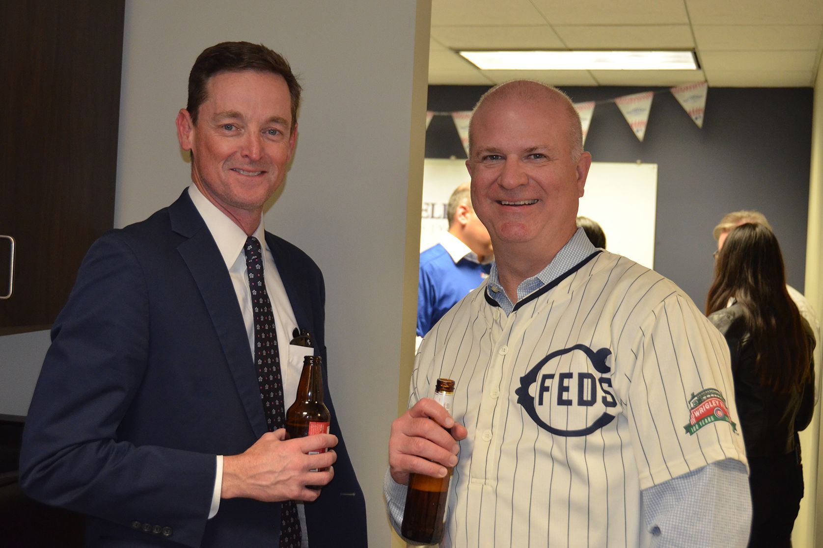 Two men are standing next to each other holding beer bottles . one of the men is wearing a feds jersey.