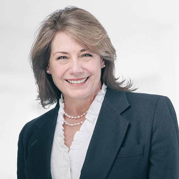 A woman in a suit and pearls smiles for the camera